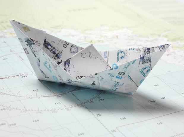 Origami paper boats made of British pounds on a nautical chart